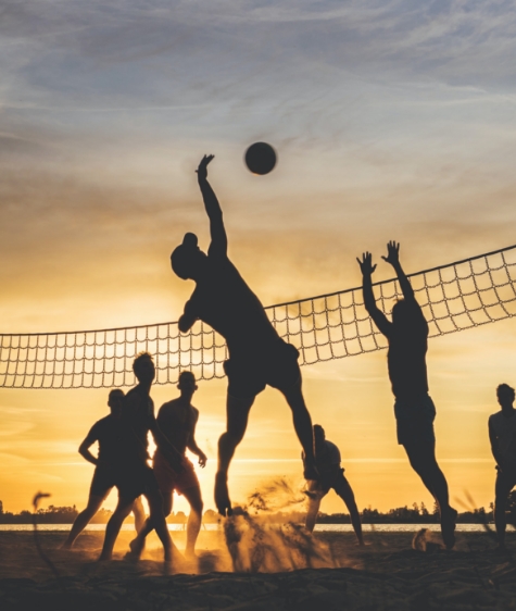 A silhouette of people playing beach volleyball at sunset.