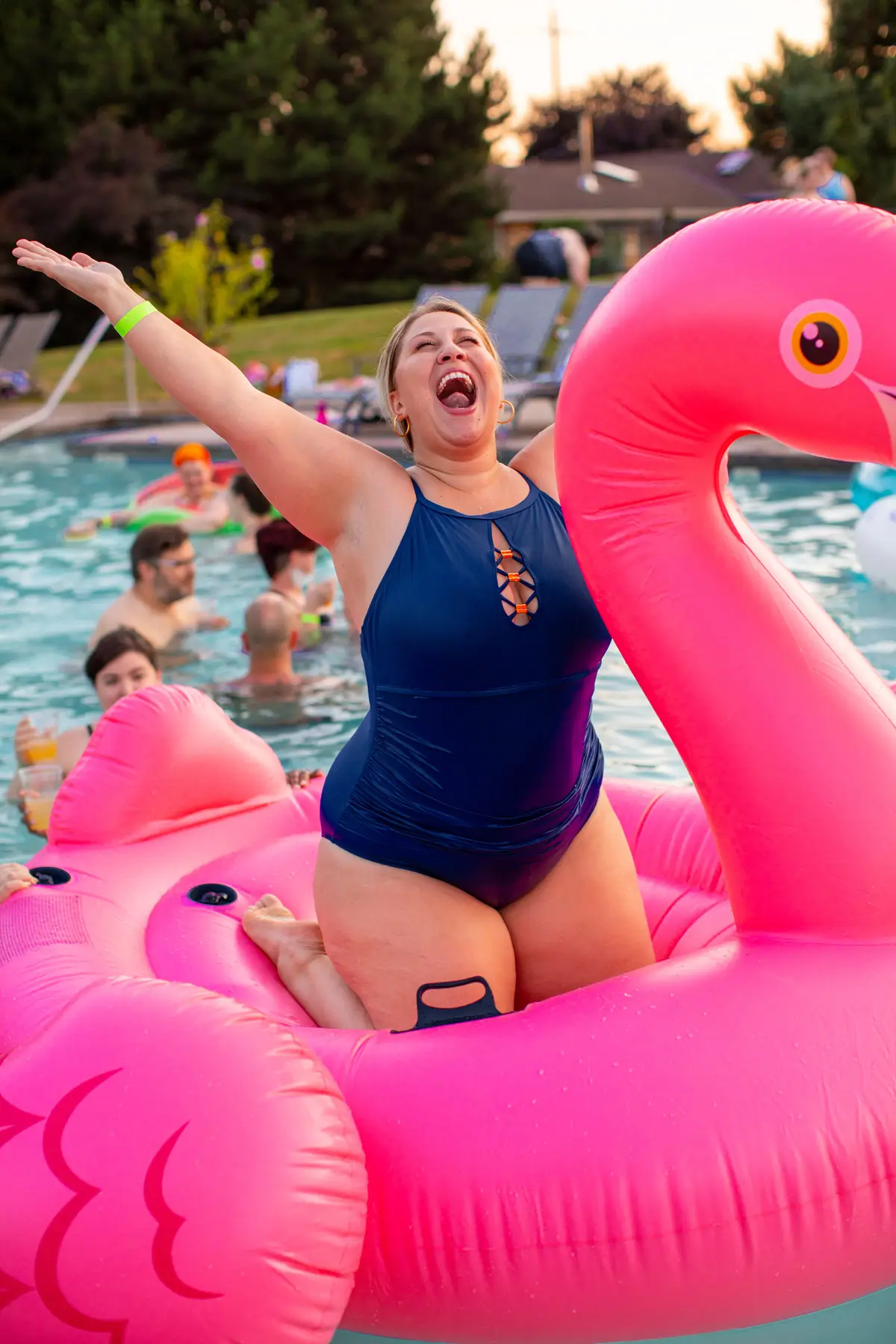 Woman happily posing on a pink flamingo pool float in a swimming pool